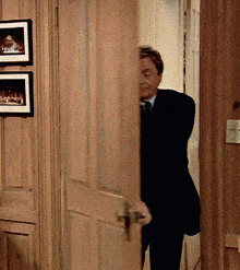 a man in a suit and tie is standing in a hallway behind a door