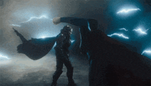 a man in a cape is fighting another man in a dark room with lightning behind them