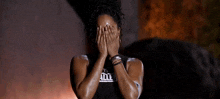 a woman is covering her face with her hands while wearing a black tank top .