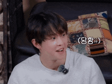 a young man sitting on a couch with a patchwork pillow and a foreign language written on his face