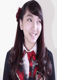 a girl in a school uniform is smiling and wearing a red and black plaid shirt and tie .