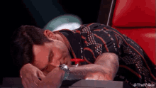 a man is laying on a red chair with his head on a button .