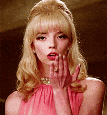 a woman wearing a pink dress has her hand on her face