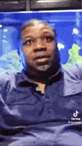 a man in a blue shirt is sitting in front of a blue fish tank .