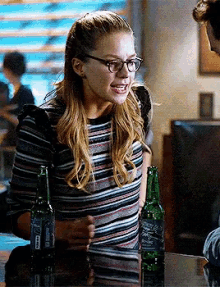 a woman wearing glasses and a striped shirt is holding a beer bottle .