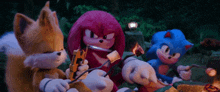 sonic , knuckles and tails are sitting around a campfire eating marshmallows .