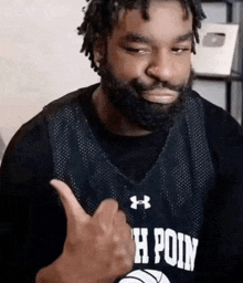 a man with a beard is wearing a black under armour basketball jersey and giving a thumbs up .