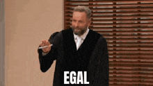 a man in a judge 's robe is standing in front of a wooden blind and holding a pen .