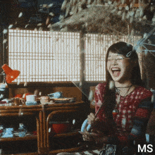 a woman in a red plaid shirt is laughing in front of a window with ms written on it