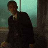 a man in a suit is standing in front of a window smoking a cigarette .