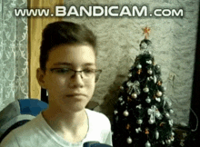 a young boy wearing glasses is sitting in front of a christmas tree ..