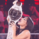 a woman is licking a championship belt while holding it in her hand .