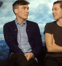 two men are sitting next to each other with their arms crossed and smiling