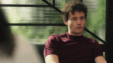 a man with curly hair is wearing a burgundy shirt
