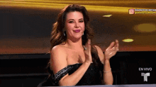 a woman in a black dress is clapping her hands in front of a screen that says en vivo
