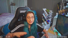 a girl with blue hair and glasses is sitting in a sidemv chair