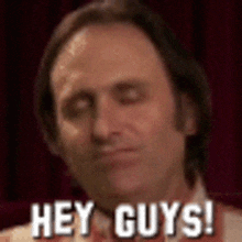 a man is standing in front of a red curtain and says hey guys !