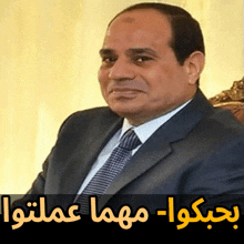 a man in a suit and tie sits in a chair with arabic writing above him