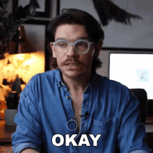 a man wearing glasses and a denim shirt says " okay "