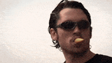 a man wearing sunglasses and a black shirt is eating something