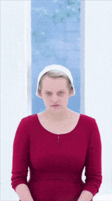 a woman wearing a red dress and a white hat is sitting in front of a window