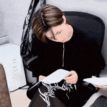 a man in a black sweater is sitting in a chair and writing on a piece of paper