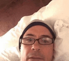 a man wearing glasses and a beanie is laying in bed