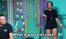 a man and a woman are standing in front of a wall of beads and the woman is saying " what a waste of cake "
