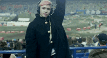 a woman wearing headphones and a black coat stands in front of a crowd