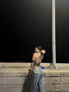 a woman in a leopard print top and jeans leans against a wall at night