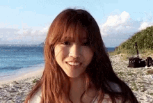 a woman with long red hair is standing on a beach smiling at the camera .