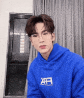 a young man wearing glasses and a blue hoodie is looking at the camera