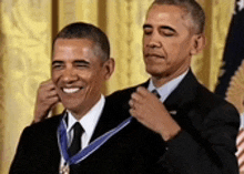 barack obama is wearing a medal around his neck while another man adjusts his tie .