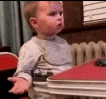 a baby is sitting at a table with his hand out .