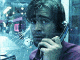 a man is talking on a pay phone with a broken glass window behind him