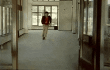 a man in a red jacket is walking through an empty hallway