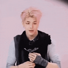 a young man with pink hair is wearing a black vest and gloves and holding a flower .
