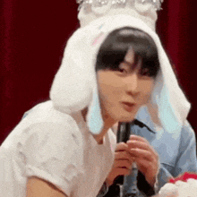 a young man wearing a bunny hat is holding a microphone .
