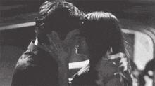 a black and white photo of a man and a woman kissing in a car .