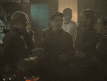 a group of men are gathered in a dark room talking