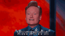 a man in a suit and tie is making a funny face in front of a red background with thai writing .