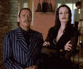 a man in a striped suit and a woman in a black dress stand next to each other