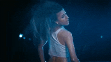a woman in a white tank top is dancing in the rain in the dark .