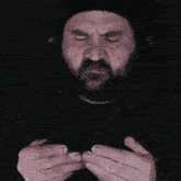 a man with a beard has his eyes closed and his hands folded in front of him