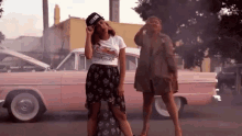 two women are standing in front of a pink car and one has a hat that says miami