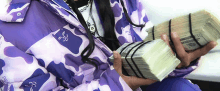 a person wearing a purple camo jacket holds a stack of money