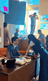 a man and a woman are sitting at a desk in a room with other people .