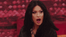 a drag queen is sitting on a couch with her mouth wide open .