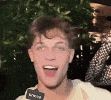 a young man wearing a tag that says prince is making a funny face .