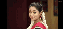 a woman in a red saree with white flowers in her hair and earrings is smiling .
